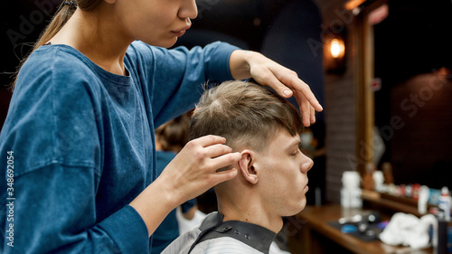 Hair Styling. Young caucasian man getting new haircut in the modern barbershop. Professional barber girl doing haircut for her client. Beauty salon