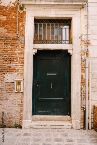 Close-ups of building facades in Venice, Italy. A wooden green front door in a stone doorway. The texture of a brick wall with communication pipes. An old intercom and a mailbox in the door.