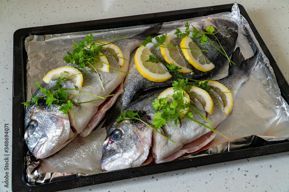 Fresh dorada fish with lemon and parsley on a baking sheet