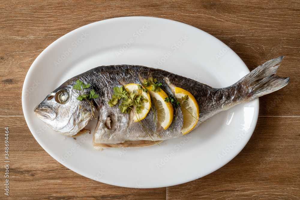 Dorada fish fried with lemon and parsley on a white plate