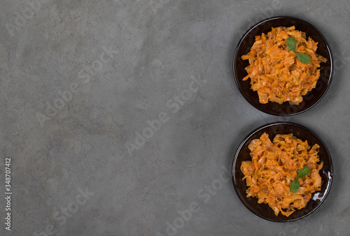 Stewed cabbage with carrots, onions and tomatoes on a plate on a dark background top view