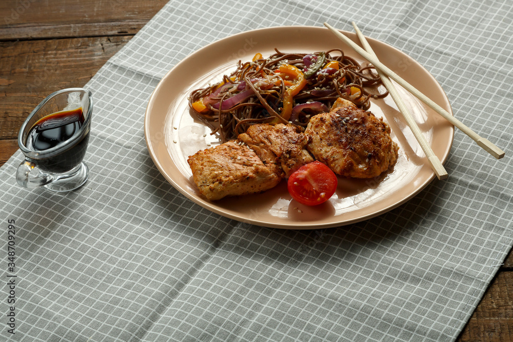 Buckwheat soba noodles with vegetables and Asian-style chicken chop on a linen napkin. Buckwheat soba noodles with vegetables and Asian-style chicken chop on a linen napkin.