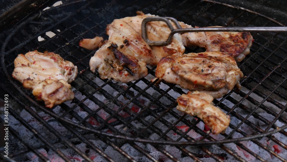 Man's hand using tongs For turning chicken meat on the barbecue grill.