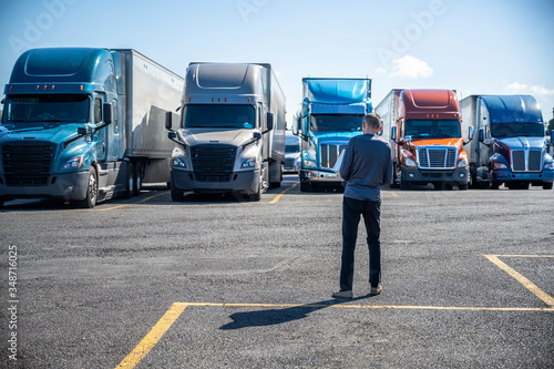Truck driver carries a shopping box in his hands and going to his big rig semi ruck parked on the truck stop parking lot photo