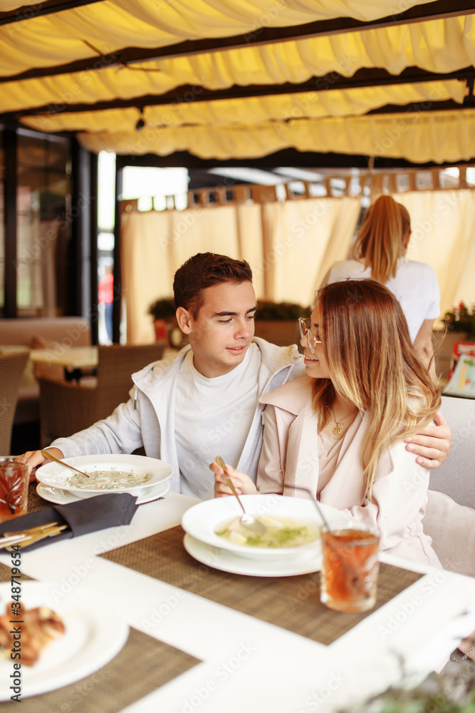 A cheerful and beautiful couple are relaxing on a summer terrace in a restaurant with food and drinks. The guy and the girl have fun on the terrace A cheerful and beautiful couple are relaxing on a summer terrace in a restaurant with food and drinks. The guy and the girl have fun on the terrace