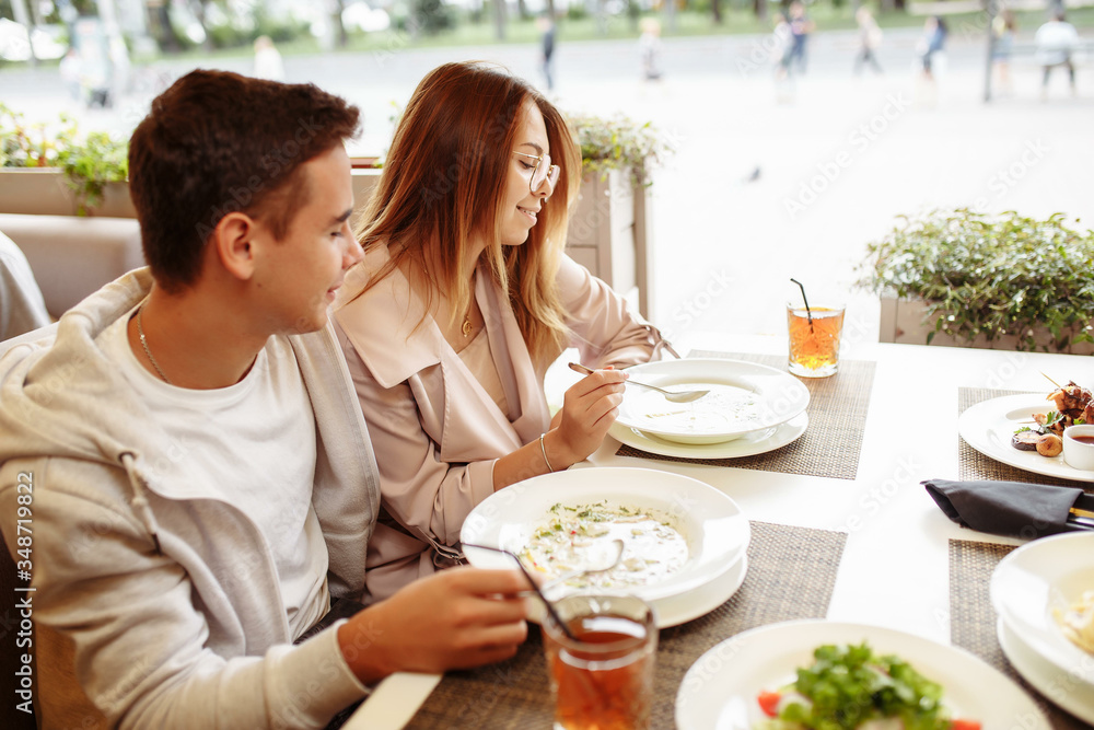 A cheerful and beautiful couple are relaxing on a summer terrace in a restaurant with food and drinks. The guy and the girl have fun on the terrace