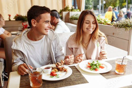 A cheerful and beautiful couple are relaxing on a summer terrace in a restaurant with food and drinks. The guy and the girl have fun on the terrace © Дмитрий Скорина