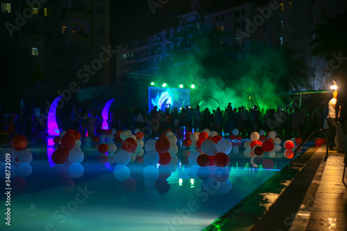 Fototapeta Naklejka Na Ścianę i Meble -  Decorated pool by the hotel. Blurred silhouette of people from the concert. bright lights. Rest in hot countries.