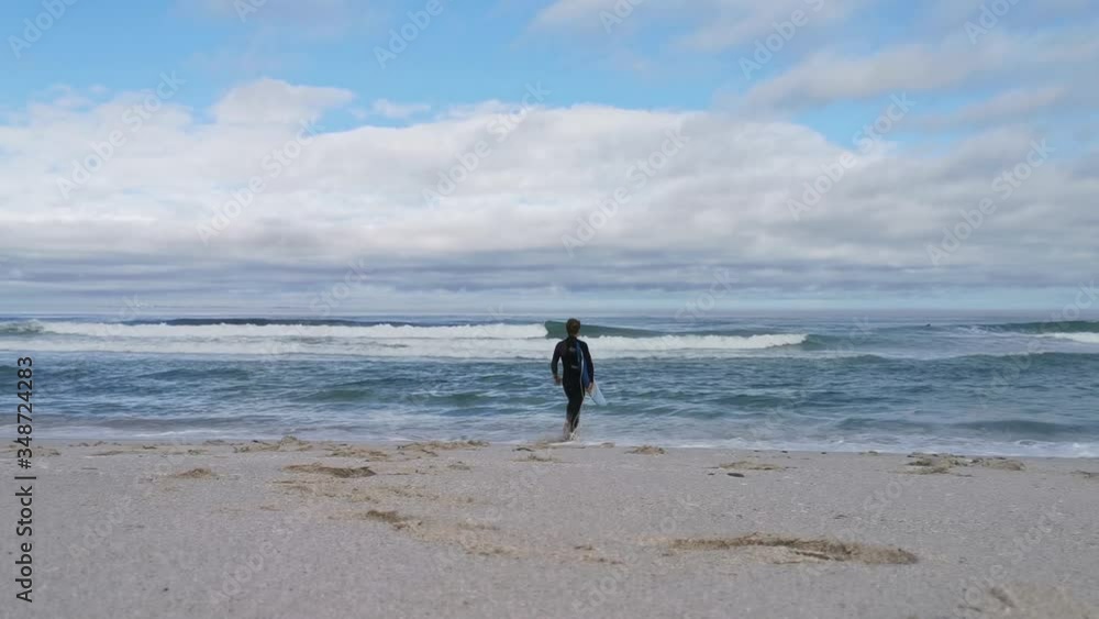 A surfer clutching his board on the beach about to wade into the ocean A surfer clutching his board on the beach about to wade into the ocean