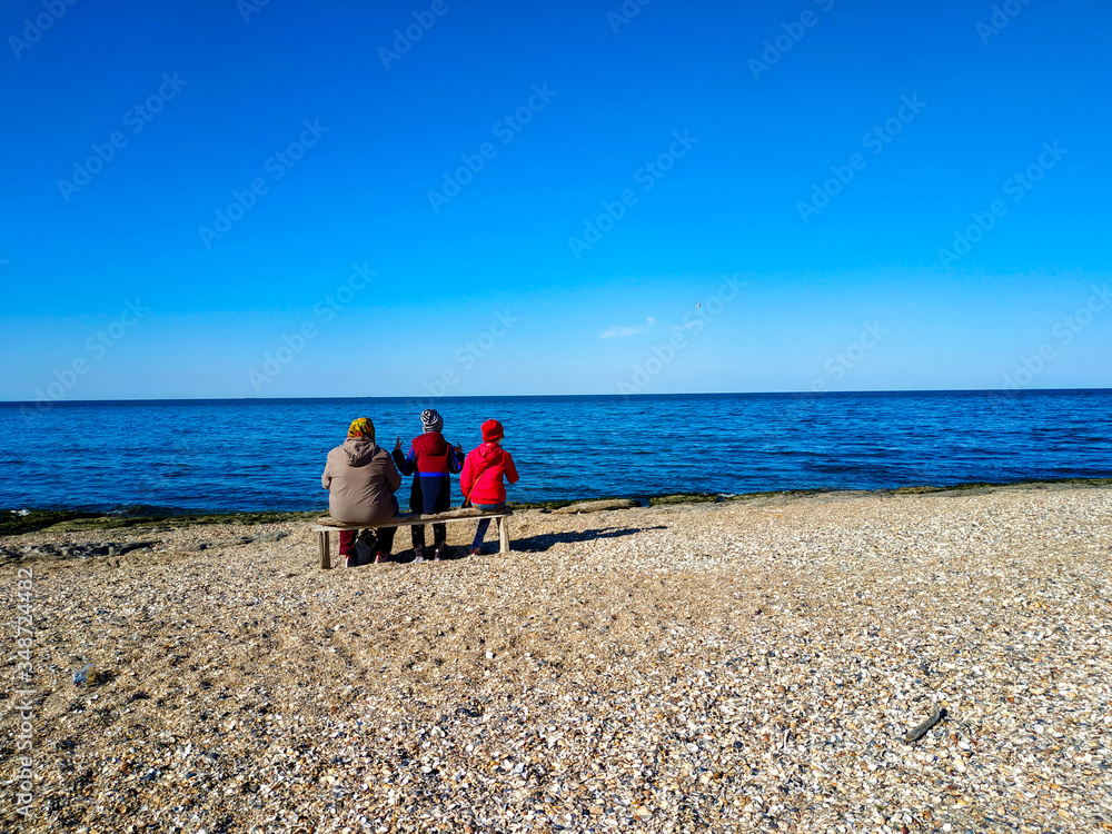 A family sitting on a bench on the beach and look on the sea with clean blue sky. A family sitting on a bench on the beach and look on the sea with clean blue sky.