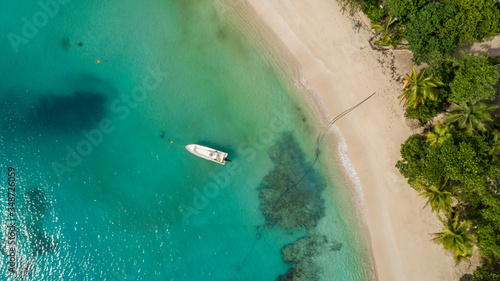 Fototapeta Naklejka Na Ścianę i Meble -  Aerial shot looking down onto boat in crystal clear aquamarine water and deserted white sandy beach