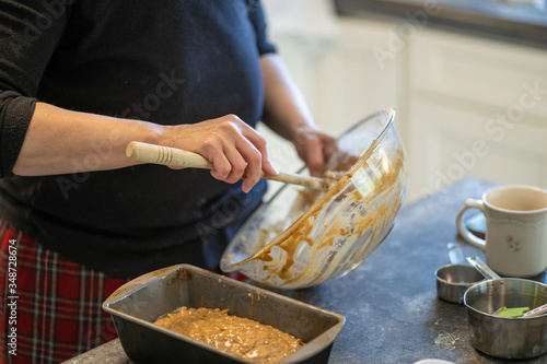 Bowl of cake bread batter in a big glass bowl with a wooden spoon being scraped into metal loaf pan.