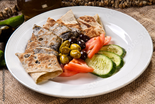Plate of traditional arabic wraps with vegetables and olives.