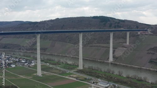 Hochmoselbrücke High Moselle Bridge in Rhineland-Palatinate Germany with cars and trucks on a freeway highway cinematic panorama rising aerial drone shot on a sunny cloudy day 30p photo