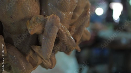 Raw plucked fresh whole chicken hanging up for sale at Asian food market, closeup photo