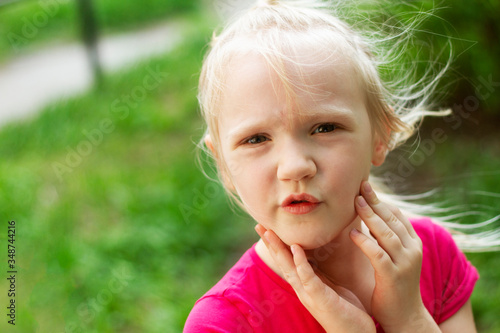 Portrait of pretty blond toddler girl in a windy summer day trying to hold her fluterring hair. Copy space