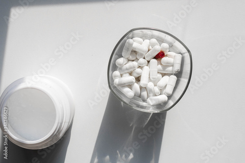 Full glass top view of pills or medicinal white capsules. Hard shadows on the white background photo