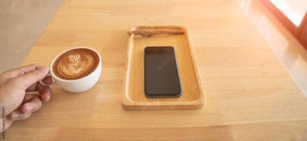 A man with a coffee cup On the table there is a mobile phone in the cafe.