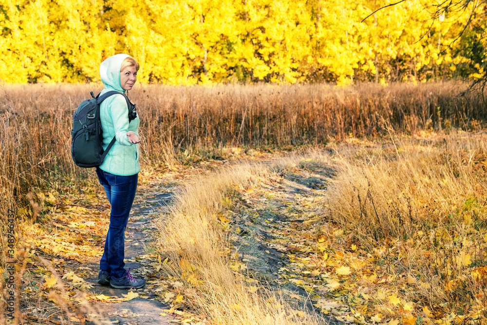 Girl with backpack invitingly reaches out for walk through autumn forest