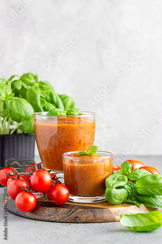 Summer homemade cold tomato cream soup in glass. Traditional Spanish soup gazpacho with basil. Grey concrete background.