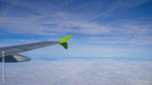 Airplane. A beautiful wing of an airplane flying high in the sky, above clouds, small towns, forests and fields. Closeup. Travel, tourism and vacation concept.For design. 