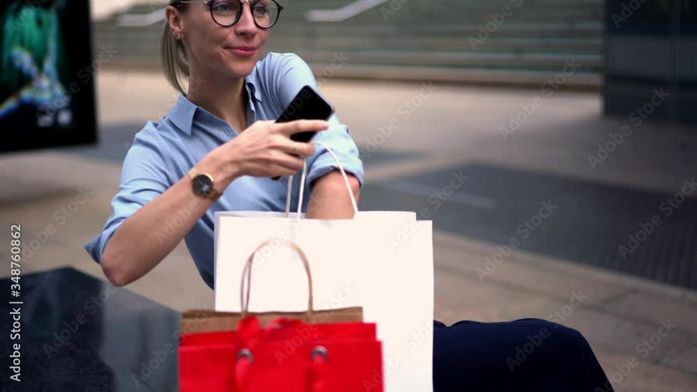 Happy young woman in eyeglasses blocked smartphone device and looking at clothes in shopping bags.Positive hipster girl dressed in fashionable clothes sitting outdoors in urban setting
Happy young woman in eyeglasses blocked smartphone device and looking at clothes in shopping bags.Positive hipster girl dressed in fashionable clothes sitting outdoors in urban setting