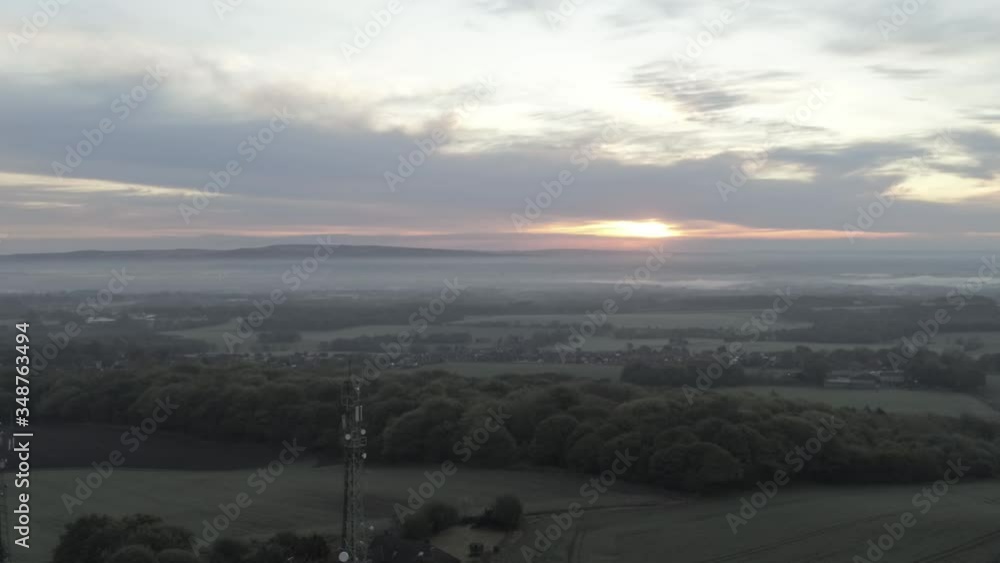 Drone aerial view rising above British misty rural farm countryside broadcast signal towers at sunrise Drone aerial view rising above British misty rural farm countryside broadcast signal towers at sunrise