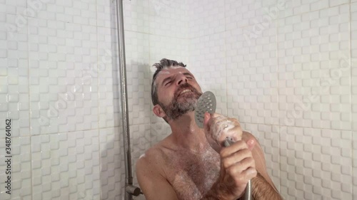  funny shot of young attractive and happy man with beard dancing and singing in the shower carefree and crazy at home pretending holding a microphone enjoying