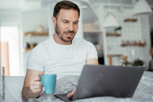 Young man watching movie in bed. Handsome man enjoying in morning. 