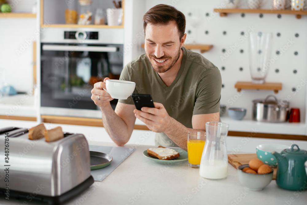 Handsome man preparing breakfast at home. Young man using the phone in kitchen. Handsome man preparing breakfast at home. Young man using the phone in kitchen.