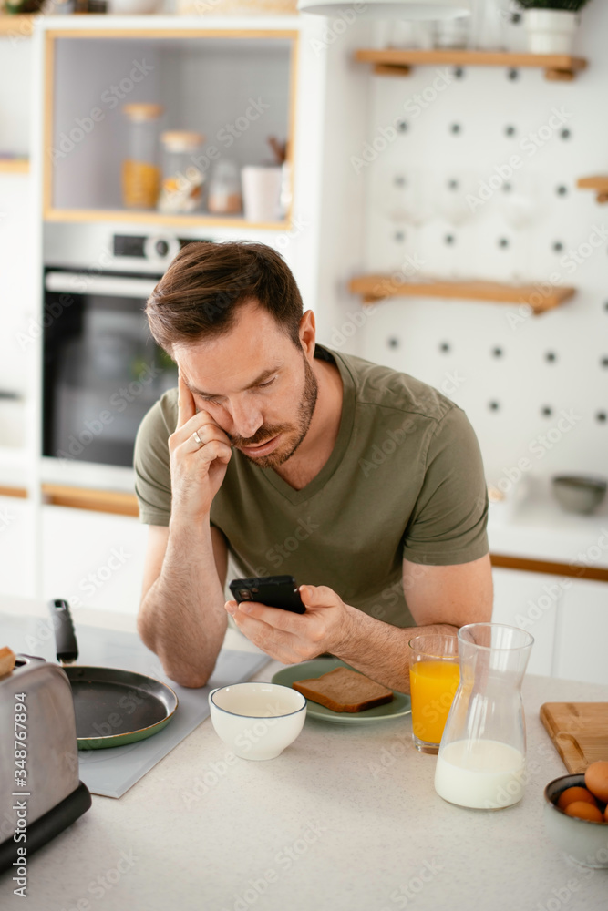 Handsome man preparing breakfast at home. Young man using the phone in kitchen. Handsome man preparing breakfast at home. Young man using the phone in kitchen.