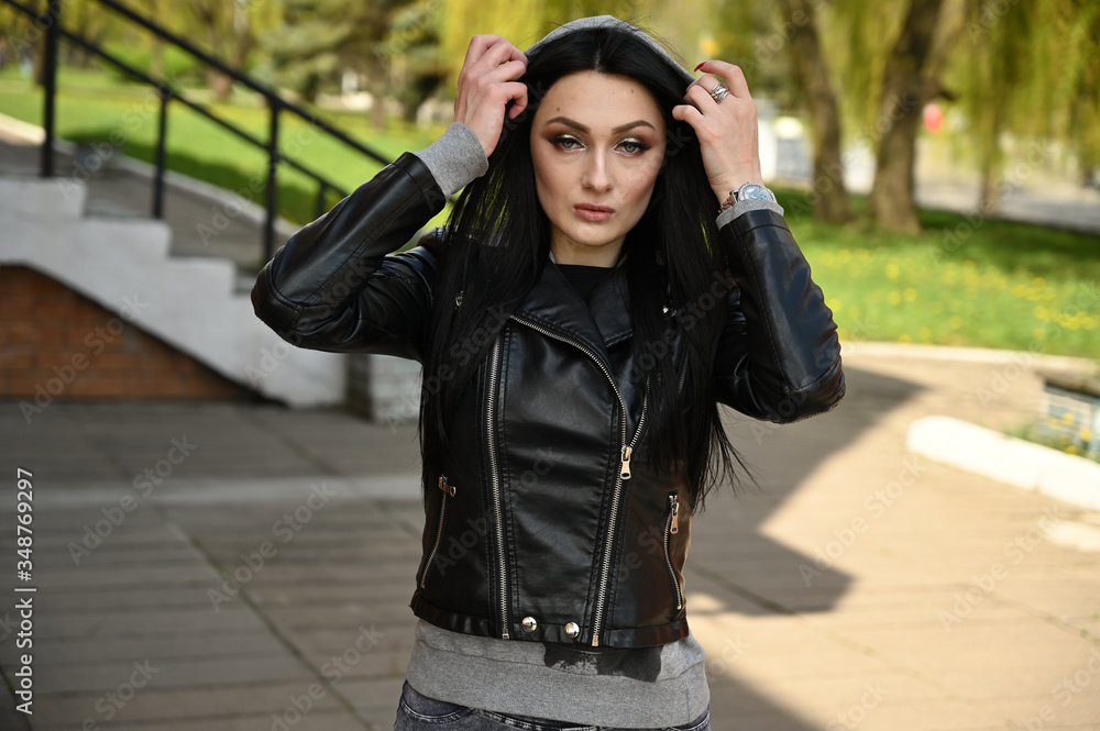 Close-up portrait in spring weather outdoors, caucasian brunette girl in jeans and a black jacket with a great figure. Model posing against the backdrop of a city park. Close-up portrait in spring weather outdoors, caucasian brunette girl in jeans and a black jacket with a great figure. Model posing against the backdrop of a city park.