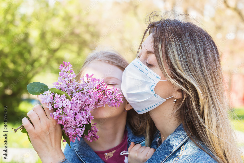 Obraz premium Mom and daughter sniffing a lilac on the street. Quarantine quit concept