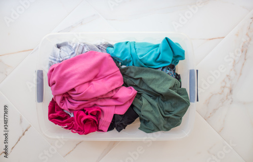  Rectangular basket with dirty linen on a white marble floor close-up, top view. Bright underwear of different colors