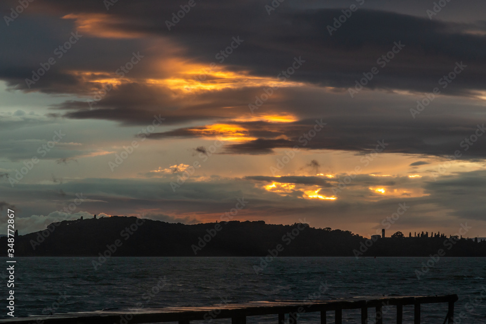 View of a pier on a lake with a ray of sun against a moody sky