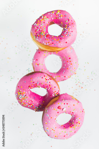 Homemade circle pink donuts with rainbow sprinkles are flying in the air levitate motion on the white background isolated. Close up top view macro shoot
