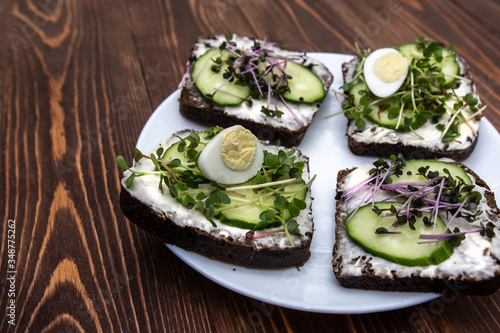 sandwiches with microgreens, cucumber and quail eggs on a white plate. wooden background. a kind of sunny glare. healthy diet. feed option. young sprouts of radish and red cabbage