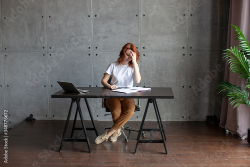 A girl in a white T-shirt is sitting at the table. Computer and open notebook. Stay at home concept. 