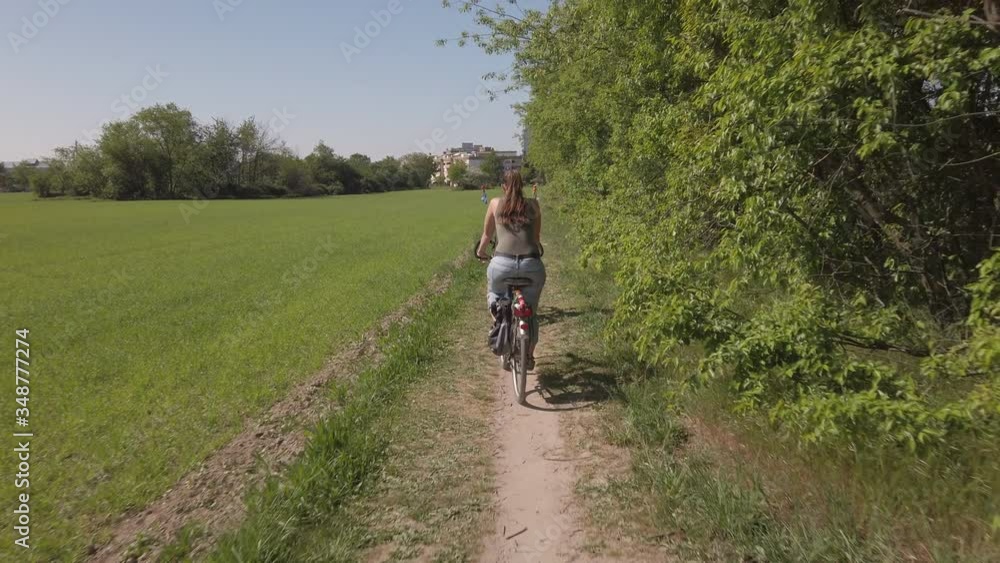 Woman being followed by the camera on a bicycle outdoors on a path in a park in western Europe Woman being followed by the camera on a bicycle outdoors on a path in a park in western Europe