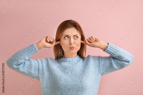 Young woman suffering from loud noise on color background photo