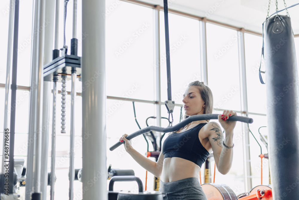 Fototapeta premium attractive athletic girl trains shoulders in simulator. view of the back muscles. healthy lifestyle.