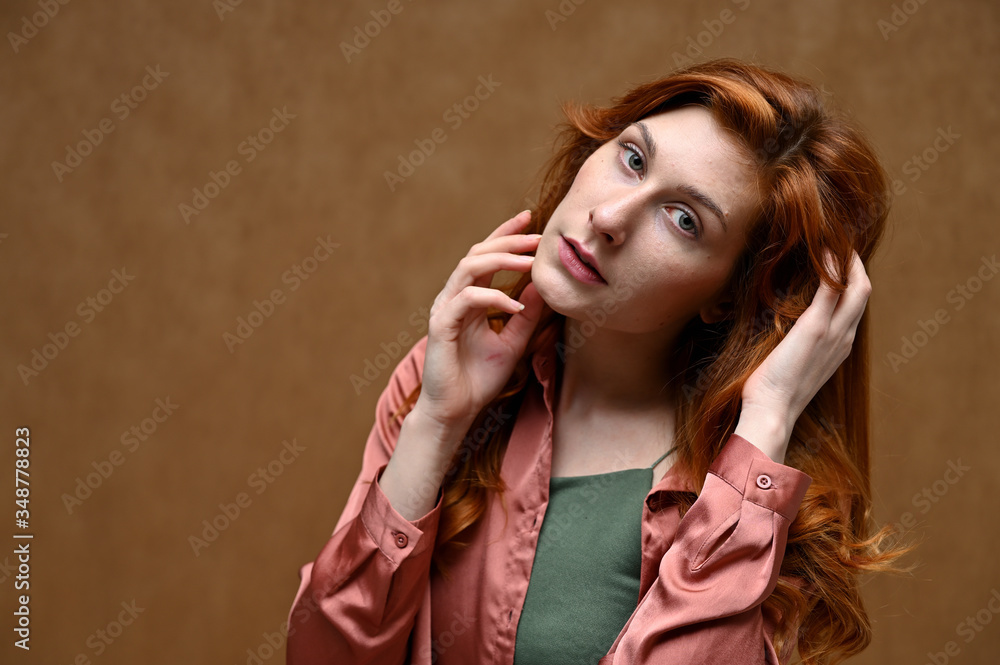 Obraz premium Studio shot with even emotions. Photo portrait on a beige background of a caucasian calm pretty young woman in a pink shirt with long beautiful red hair.