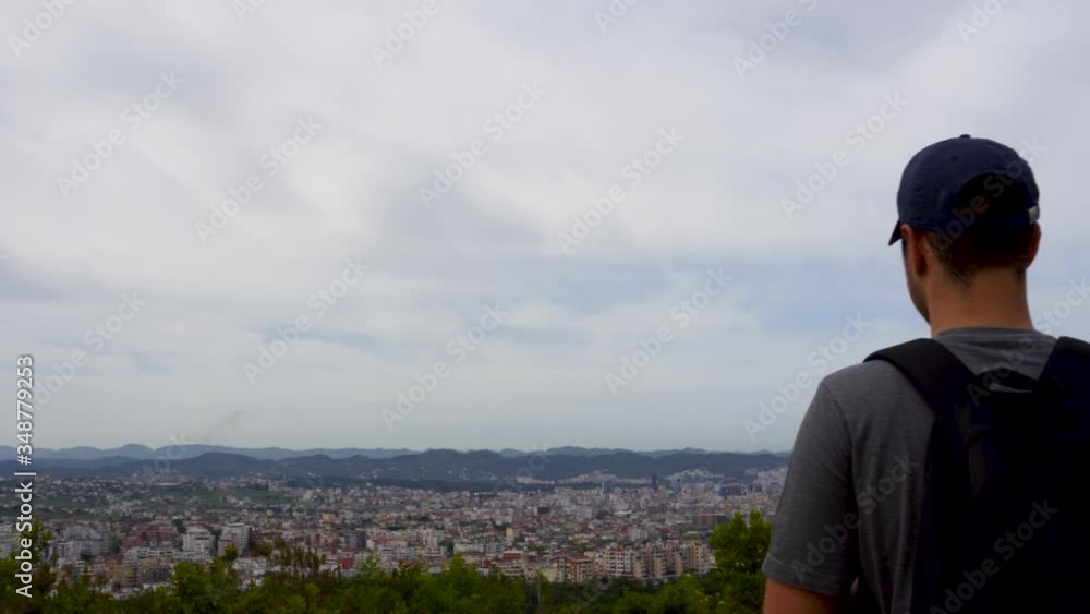Hiking boy watching city buildings in horizon after coming from mountain on a cloudy sky background Hiking boy watching city buildings in horizon after coming from mountain on a cloudy sky background