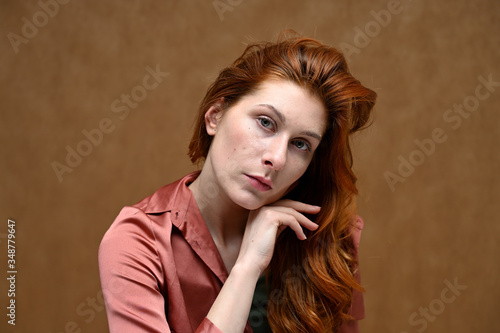 Photo portrait on a beige background of a caucasian calm pretty young woman in a pink shirt with long beautiful red hair. Studio shot.