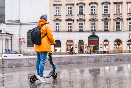 man in yellow raincoat riding by city street at electric scooter