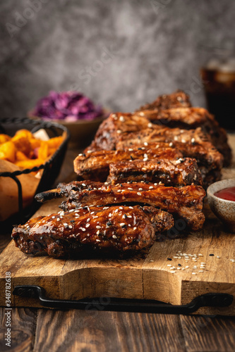 Barbecue pork ribs on a wooden board  potato wedges  burger and cola glass  sause. Fast food. Close-up  copy space.