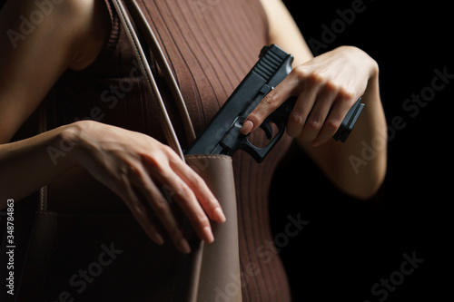 Woman hand pulling a pistol out of handbag on black background.