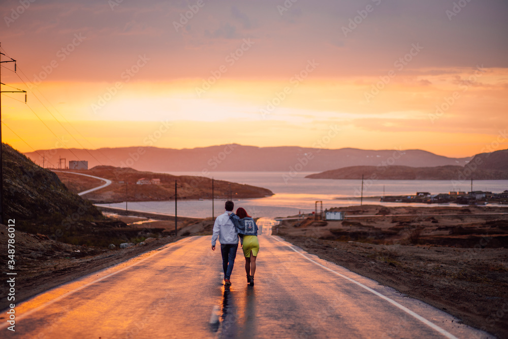 Young couple on the way to the Barents Sea on a wet road in a sunset Young couple on the way to the Barents Sea on a wet road in a sunset