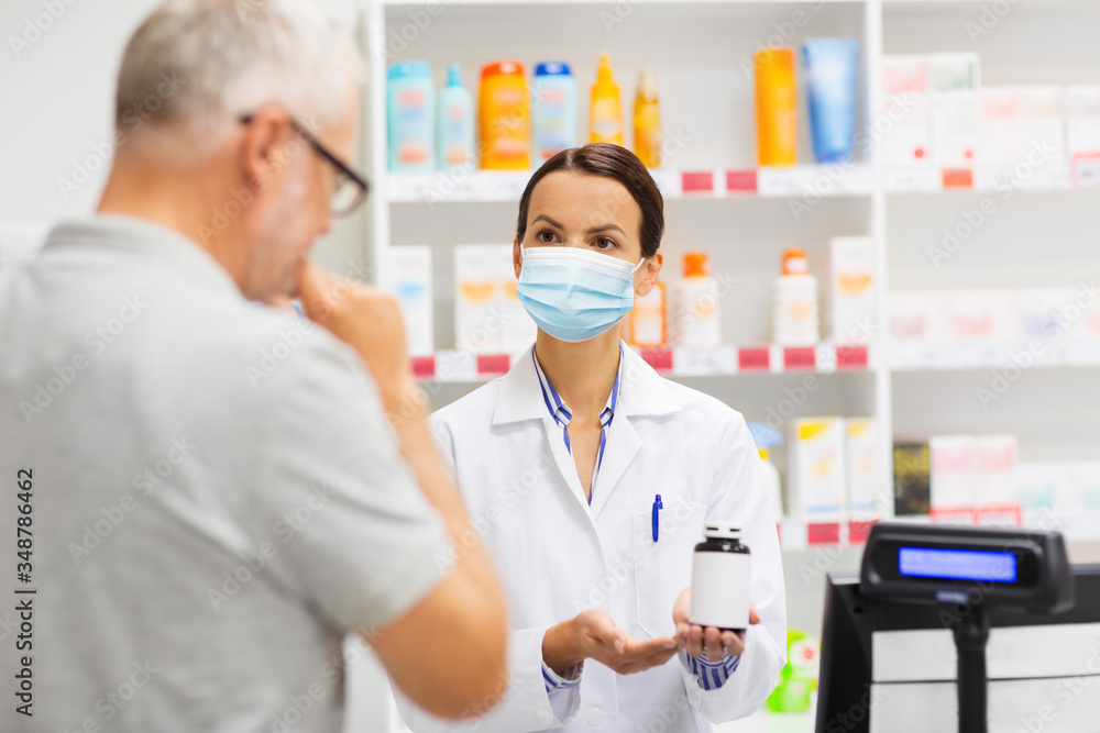 Obraz premium medicine, pharmaceutics, health care and people concept - apothecary wearing face protective medical mask for protection from virus disease showing drug to senior man customer at drugstore