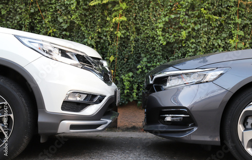 Closeup of front side of white and grey cars  parking in the opposite direction with natural background.  © Amphon
